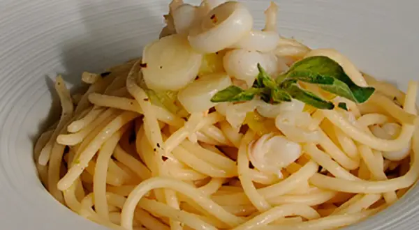 Deliciosos espaguetis con calamares, un plato de pasta con trozos de calamar y hojas verdes, servido en un cuenco blanco.