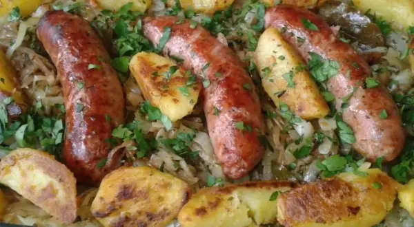 Pyszna biała kiełbasa z kapustą kiszoną i pieczonymi ziemniakami, posypana natką pietruszki.
