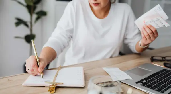 Mujer revisa facturas y escribe en agenda. El heredero no paga gastos vivienda, pero ella organiza las finanzas.