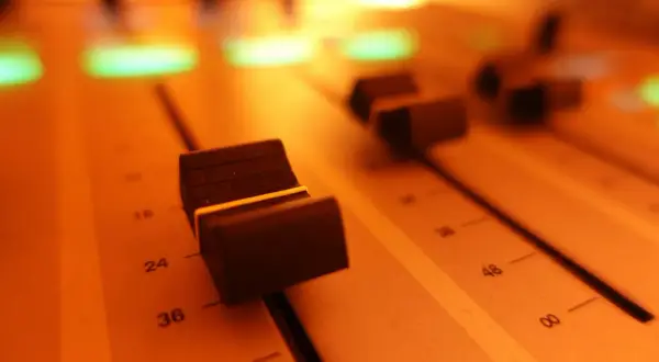 Suwaki miksera audio, oświetlone ciepłym, pomarańczowym światłem. To miejsce, gdzie rodzi się dźwięk.
