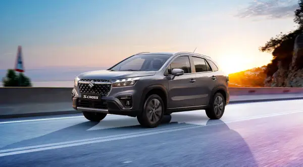 Grå Suzuki S-Cross kör längs en väg vid solnedgången. Inga problem här, bara en vacker resa.