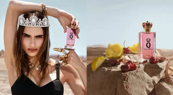 Królowa w koronie i biżuterii trzyma flakon perfum Dolce & Gabbana Q. Obok, na kamieniu, leżą wiśnie i cytryny.