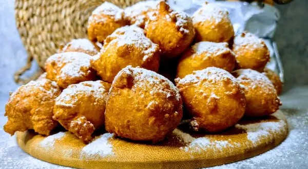 Puszyste pączki z serków homo, posypane cukrem pudrem, wyglądają jak śnieżne kule na drewnianej desce.