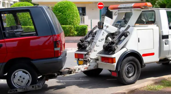 Une dépanneuse enlève une voiture rouge. Une amende pour stationnement illégal a peut-être été émise.