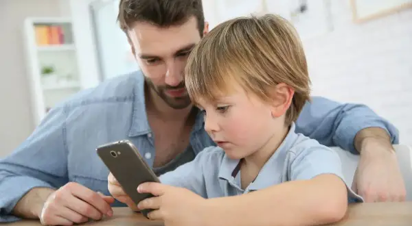 Tata pokazuje synowi jego pierwszy telefon dla dziecka. Chłopiec z zaciekawieniem ogląda ekran.