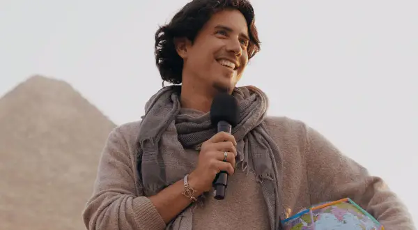 Matias de Stefano, con un micrófono y un globo terráqueo, sonríe ante una pirámide.