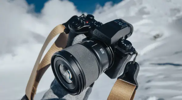 Czarne body aparatu Lumix z obiektywem i beżowym paskiem na tle zaśnieżonych gór.