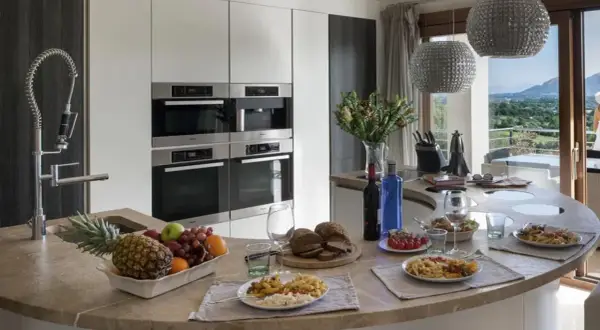Cocina moderna con encimera curva, electrodomésticos integrados y vista al paisaje. Ideal para un contrato de alquiler temporal, con comida servida y frutas frescas.