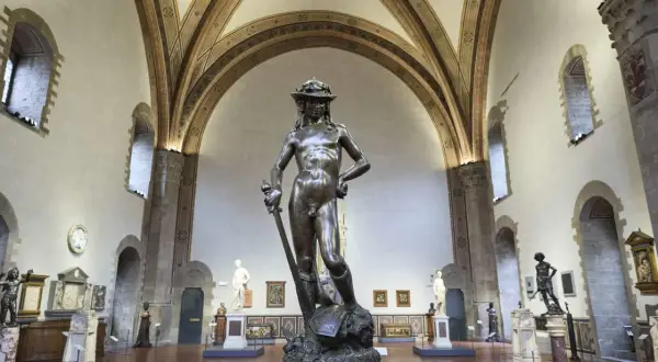 Donatello's David, a bronze masterpiece, stands triumphantly in a grand hall, surrounded by other sculptures and art.