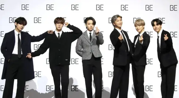 Sechs junge Männer, die wie eine Boyband aussehen, posieren vor einer Wand mit dem Schriftzug "BE".