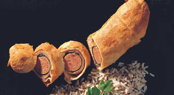 Herzhaft belegter Bratwurst im Teigmantel, aufgeschnitten und mit Reis garniert.