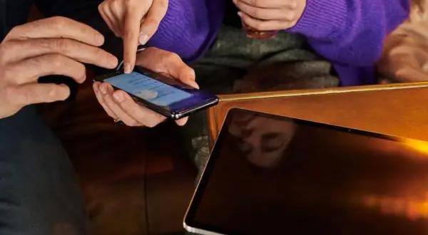 Dwie osoby sprawdzają telefon, szukając informacji, jak sprawdzić czy telefon ma wirusa. Obok leży tablet.