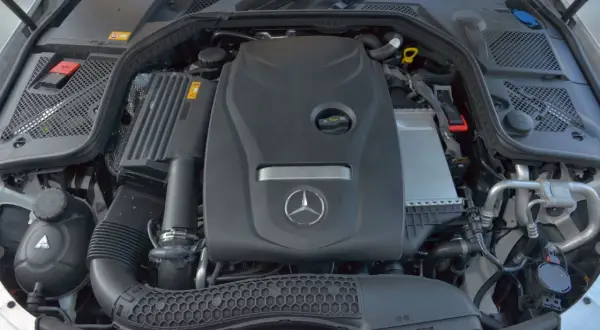 Silnik w mercedes benz klasa c. Widoczny jest czarny plastikowy wlot powietrza, zbiornik płynu chłodniczego i osłona silnika z logo producenta.