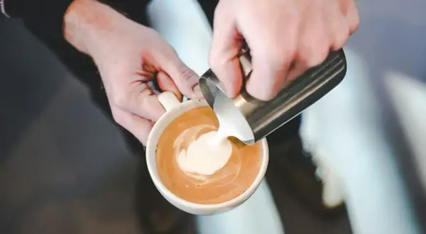 Barista versa latte art, mostrando come fare la schiuma al latte per un cappuccino perfetto.