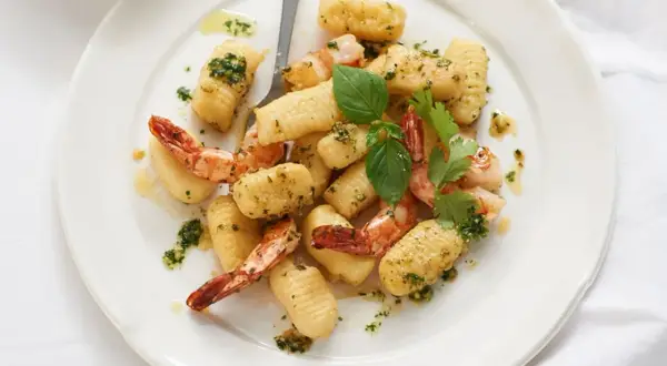 Gnocchi mit Garnelen, verfeinert mit Kräutern und Öl, auf einem weißen Teller angerichtet.