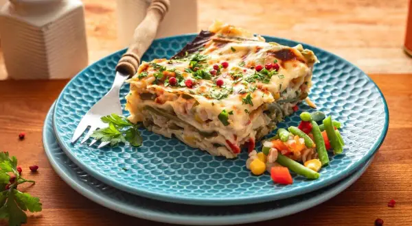 Kawałek pysznej, warzywnej lasagne na niebieskim talerzu, posypany natką i pieprzem. To bardzo dobry przepis na lazanię, który zachwyci każdego!