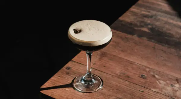 Elegancki Espresso Martini z pianką i ziarnem kawy na drewnianym stole. Idealny przepis na ten klasyczny drink.
