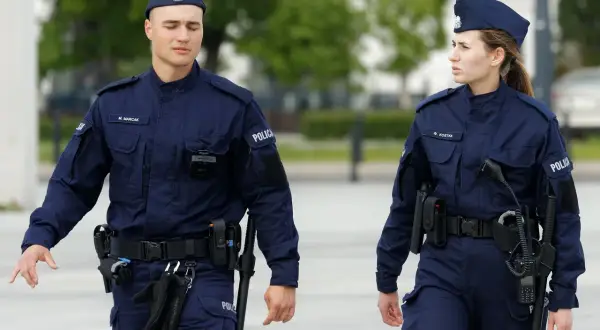 Dwóch policjantów w granatowych mundurach, z widocznymi stopniami w policji, idzie obok siebie.