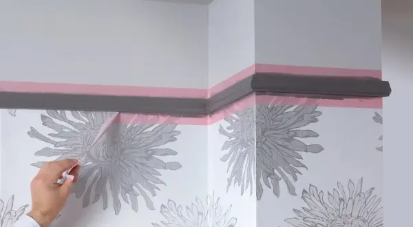Maintenant, quand enlever bande cache peinture pour une finition parfaite. Un coin de mur avec papier peint à fleurs grises et moulure peinte en gris.