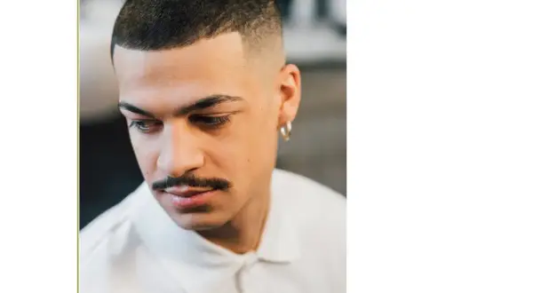 Uomo con capelli corti con linea uomo, baffi e orecchino a cerchio.