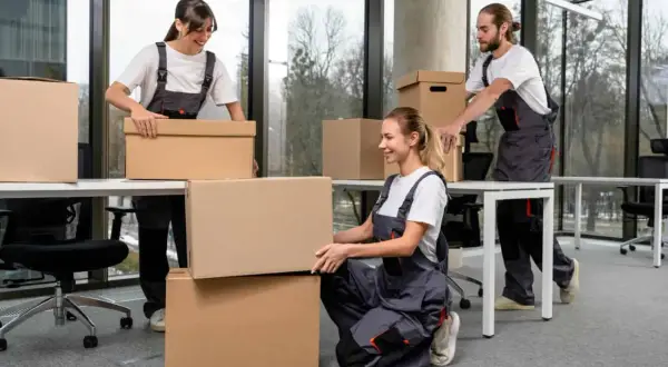 Tre persone in tuta grigia impacchettano scatole per svuotare casa.