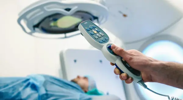 Dłoń trzymająca kontroler aparatu do radioterapii, pacjent na stole. Nowoczesna chemia biologiczna na raka.