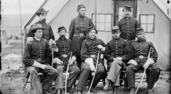 Gruppbild av nio män i uniformer från amerikanska inbördeskriget. De sitter och står framför ett tält. En enhetlig serie av militärkläder.
