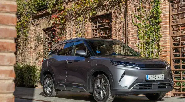 Un coche gris moderno, con matrícula 2154 NHG, aparcado frente a una pared de ladrillos cubierta de hiedra. Es el **atto 2** de la marca.