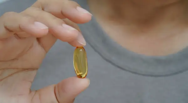 Dłoń trzyma żółtą kapsułkę. Czy suplementy omega-3 6 9 mają skutki uboczne?