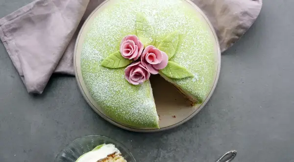 En vacker prinsesstårta med grönt marsipanlock, rosa rosor och blad. Ett stycke är uppskuret, perfekt för att inspireras av ett prinsesstårta recept.