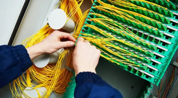 Mains de technicien travaillant sur un panneau de brassage fibre optique, gérant un câble fibre cassé.