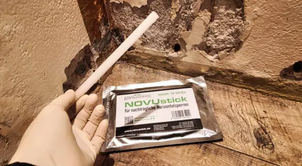 Ein Handschuh hält einen Stab, der für die nachträgliche Horizontalsperre gedacht ist. Das Produkt NOVUstick verspricht, dass man die Horizontalsperre selber machen kann.