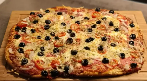 Frisch gebackene Pizza mit Tomaten, Oliven und Käse auf einem Holzbrett. Der Pizzateig wurde im Thermomix zubereitet.