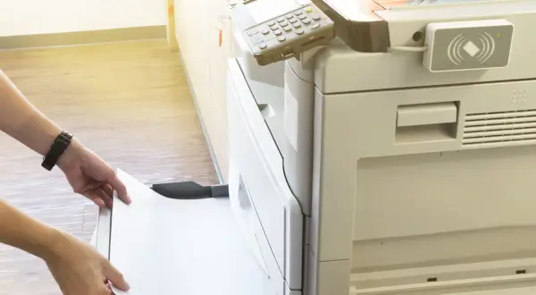 Mani inseriscono un foglio di carta in una stampante, pronta per stampare in formato super A3.