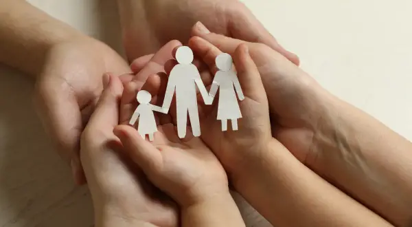 Dłonie dorosłych i dziecka trzymają papierowe figurki rodziny. Symbol wsparcia i troski, jak zasiłek rodzinny.