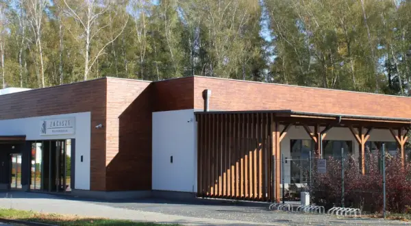 Nowoczesna restauracja Zacisze Ostrzeszów z drewnianą elewacją i przeszklonym wejściem, otoczona drzewami.