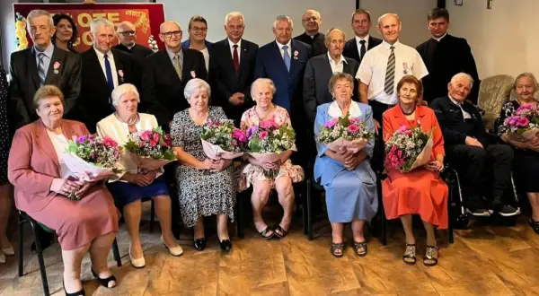 Uroczystość z okazji złotych godów. Seniorzy z bukietami kwiatów świętują 50 lat małżeństwa.