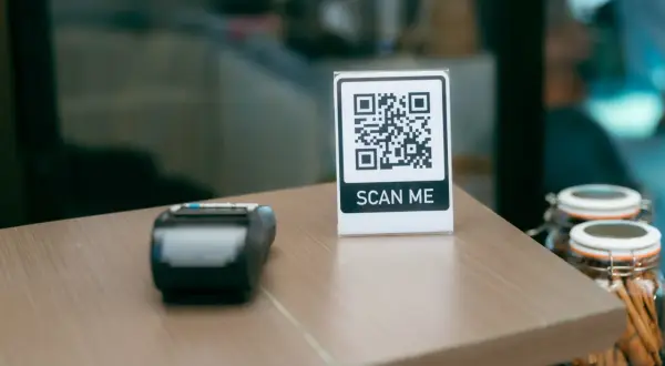Stolik z terminalem płatniczym i tabliczką "SCAN ME" pokazuje, jak sie skanuje kod QR.
