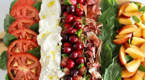 Burrata Antipasti: Tomaten, Burrata, Kirschen, Erdbeeren, Schinken und Pfirsiche auf einem Holzbrett.