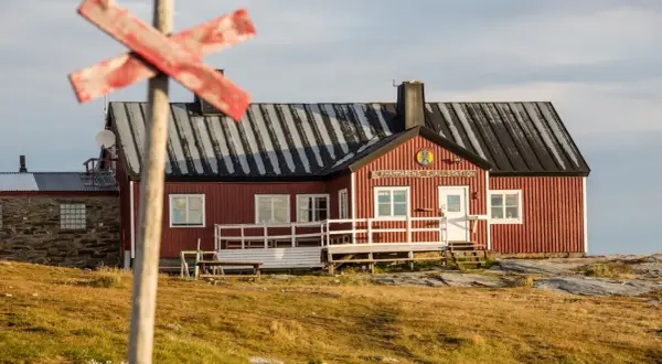 STF Blåhammaren Fjällstation, en röd fjällstuga med vita detaljer, välkomnar vandrare i ett kargt landskap.