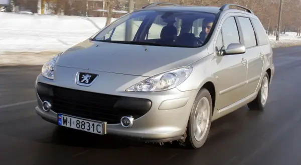 Srebrny Peugeot 307 1.6 HDI w wersji kombi jedzie po drodze, w tle zimowy krajobraz.