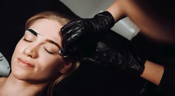 Stylist w czarnej rękawiczce nakłada hennę na brwi kobiety.