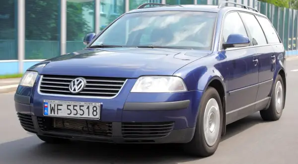 Granatowy Volkswagen Passat kombi, model b5, jedzie po drodze.