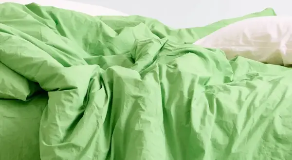 Ein Bett mit zerknitterter, leuchtend grüner Bettwäsche und einem weißen Kissen. Was ist Modal? Es ist ein Stoff, der sich so weich anfühlt.