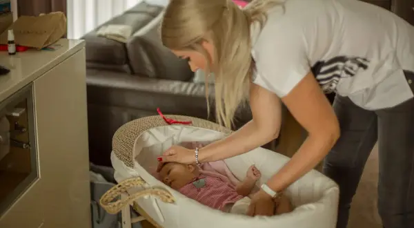 Mama delikatnie kładzie śpiące dziecko do kosza. To pierwszy krok, jak nauczyć dziecko samodzielnego zasypiania.