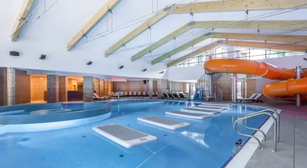 Wnętrze hotelu z aquaparkiem w górach. Basen z pomarańczowymi zjeżdżalniami, leżakami i dmuchanymi materacami.