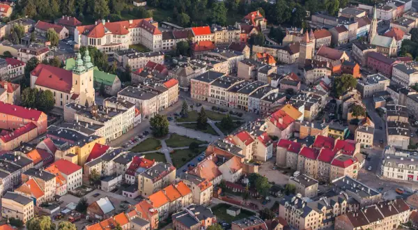 Widok z lotu ptaka na miasto z czerwonymi dachami, kościołem i placem. Może to być początek szlaku czarownic.