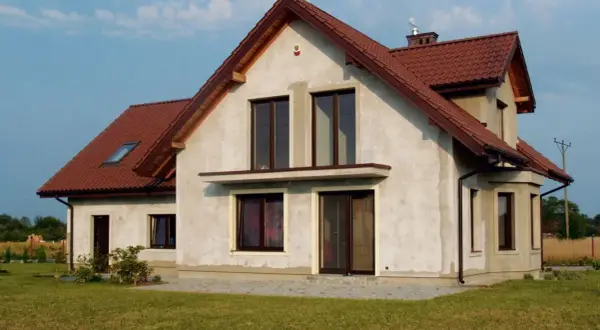 Dom w budowie z brązowym dachem, w tle linia wysokiego napięcia.