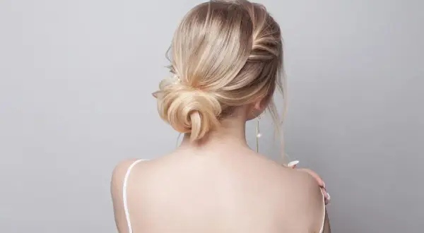 Elegancki kok z blond włosów, spięte spinką z perłą, podkreśla delikatność stylizacji.