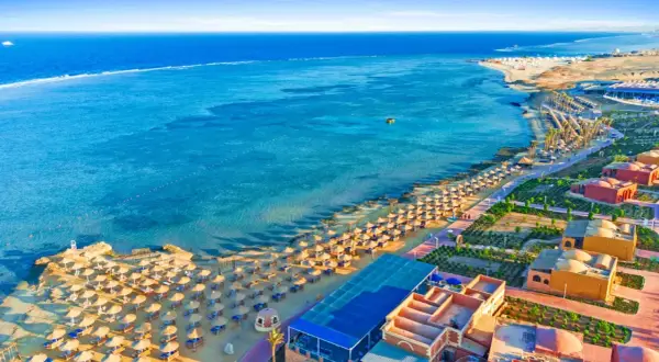 Piękna plaża z rzędami parasoli i palm, turkusowe morze i hotelowe budynki. Marsa Alam atrakcje zachwycają!